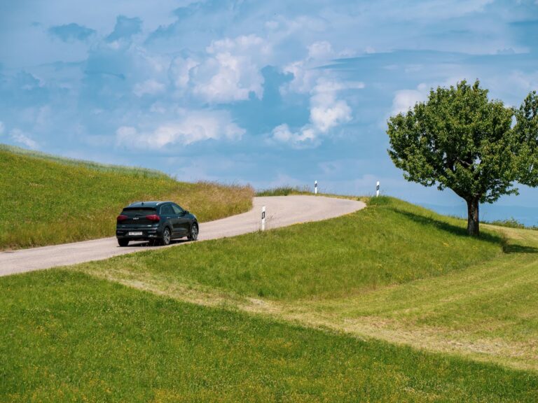 Black car cruising on a winding rural road under a blue sky with scattered clouds.