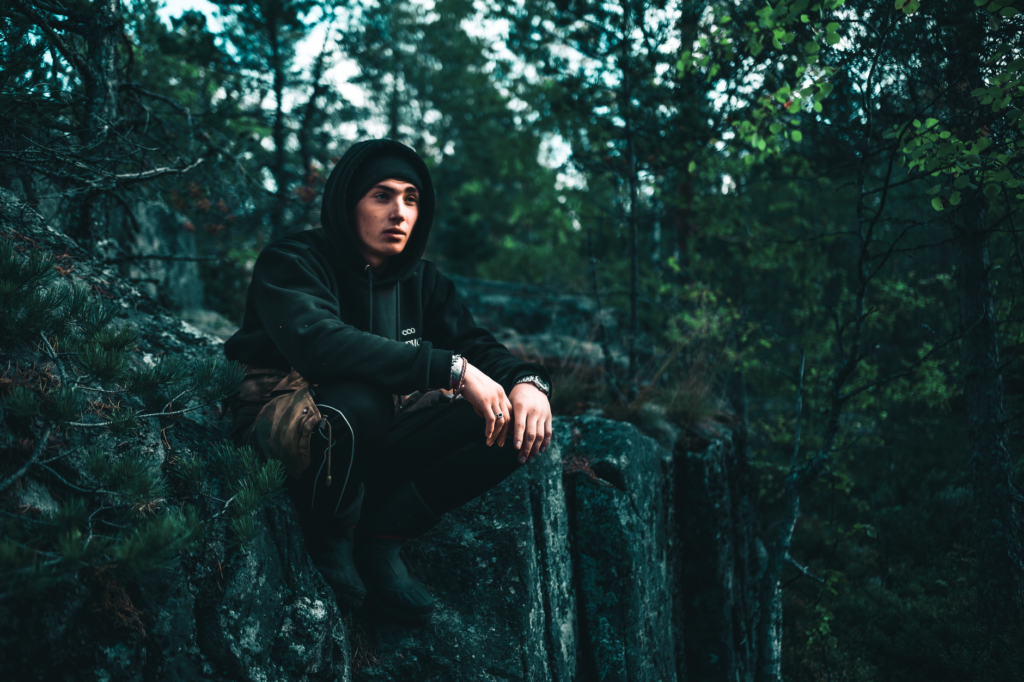 A young man sits on a forest edge rock, enjoying the tranquil natural surroundings.