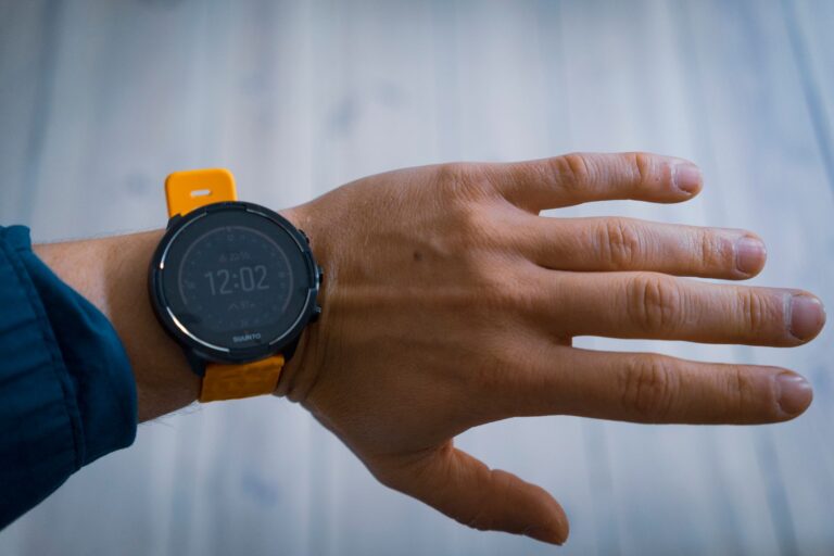 A close-up image of a smartwatch with a yellow strap worn on a wrist, displaying the time 12:02.