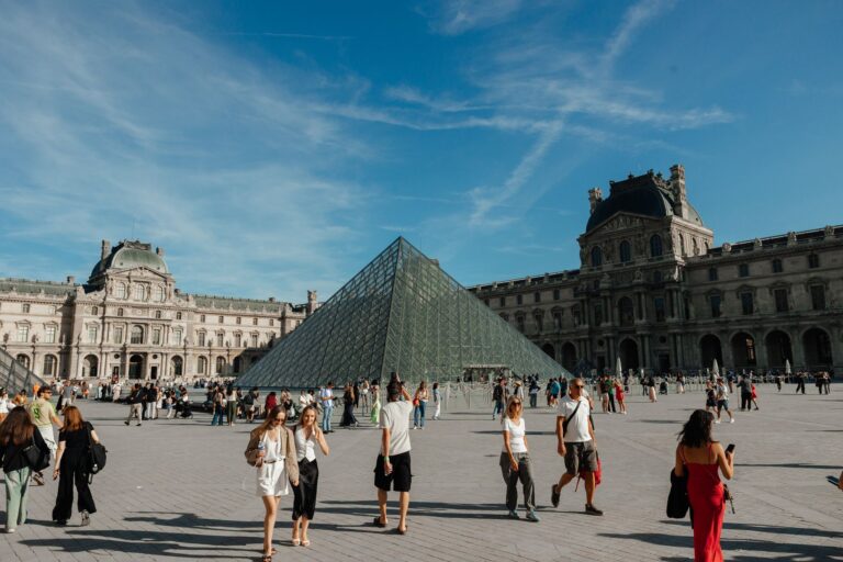 Visitors exploring the Louvre Pyramid under a clear blue sky in Paris, France.
