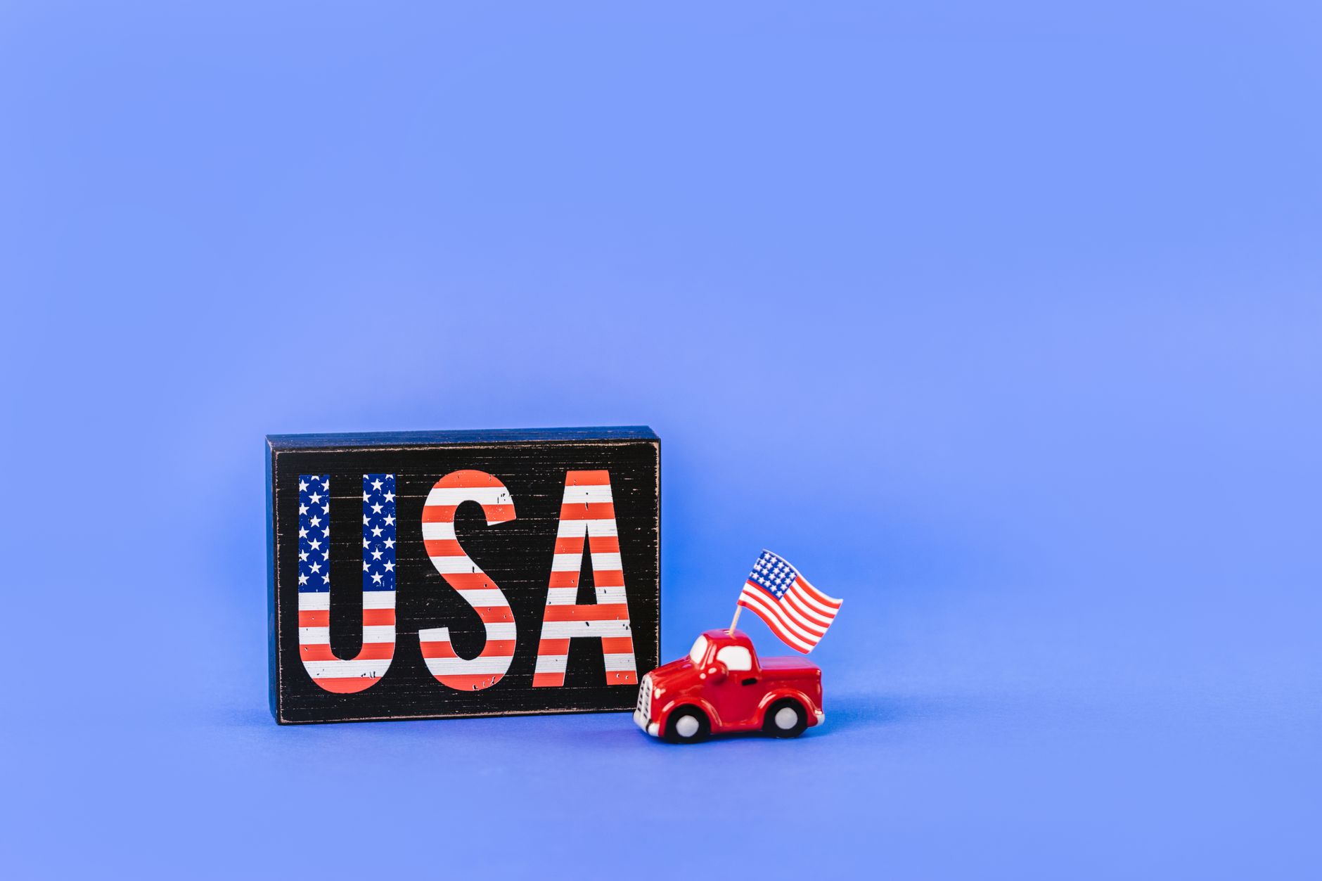 Patriotic USA sign with miniature car and American flag on blue background.