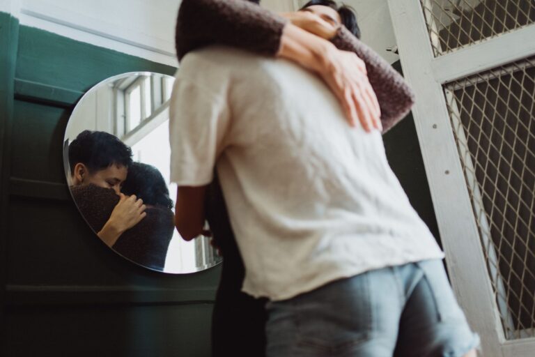 A loving embrace between two people is captured in the reflection of a circular mirror indoors.