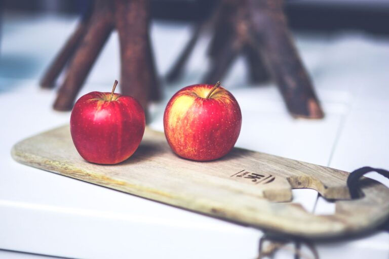 Two bright red apples displayed on a wooden board, highlighting health and freshness.